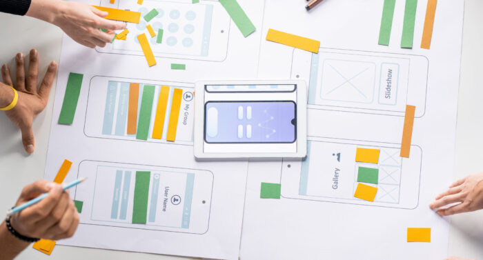 Hands of young contemporary designers of new mobile applications over papers with sketches and colorful stripes discussing working points